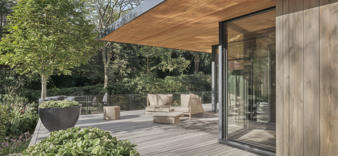 Terrasse bois moderne avec fauteuils et végétation luxuriante.