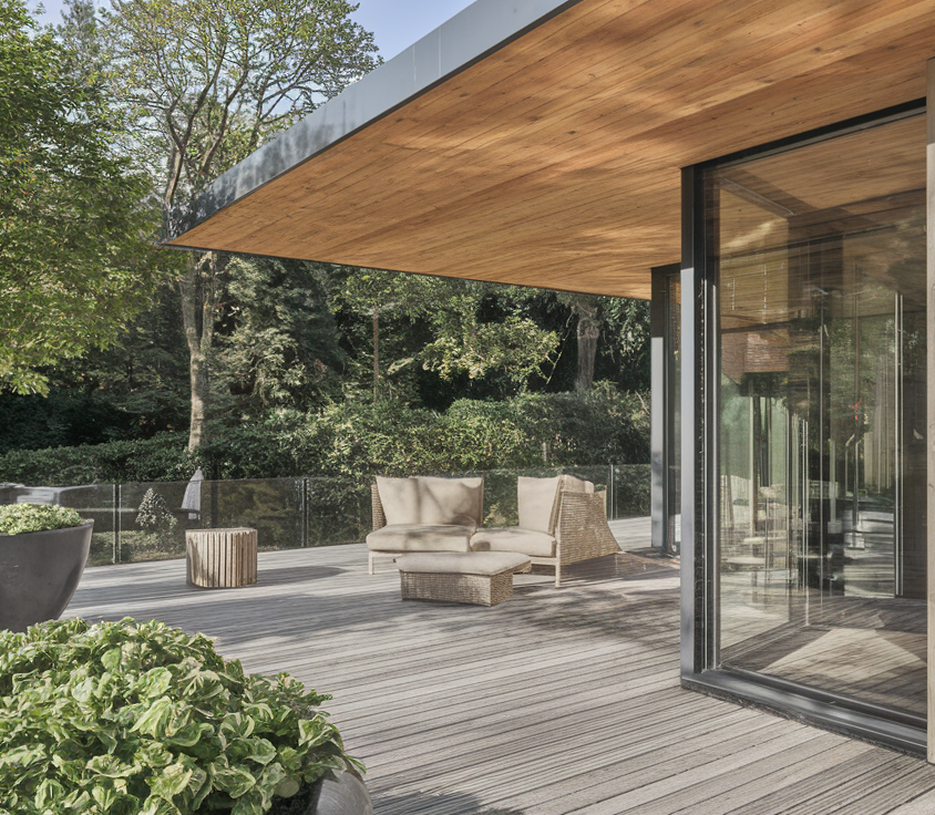 Terrasse bois moderne avec fauteuils et végétation luxuriante.