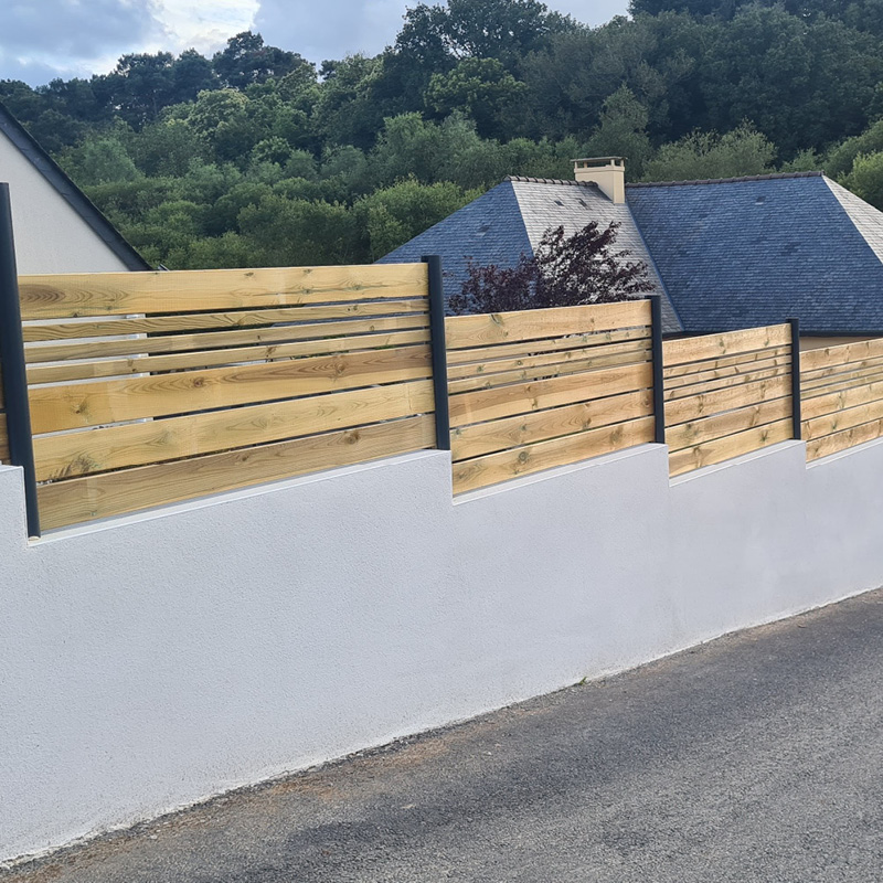 Clôture en bois devant maison et forêt.