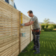 Homme installe une clôture en bois dans un jardin
