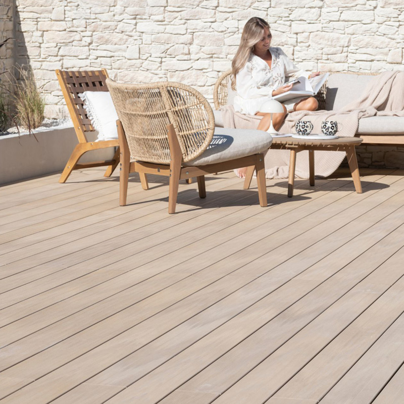 Femme lisant sur terrasse bois avec fauteuils.