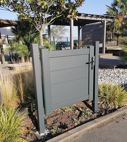 Portillon de jardin gris dans un paysage ensoleillé.