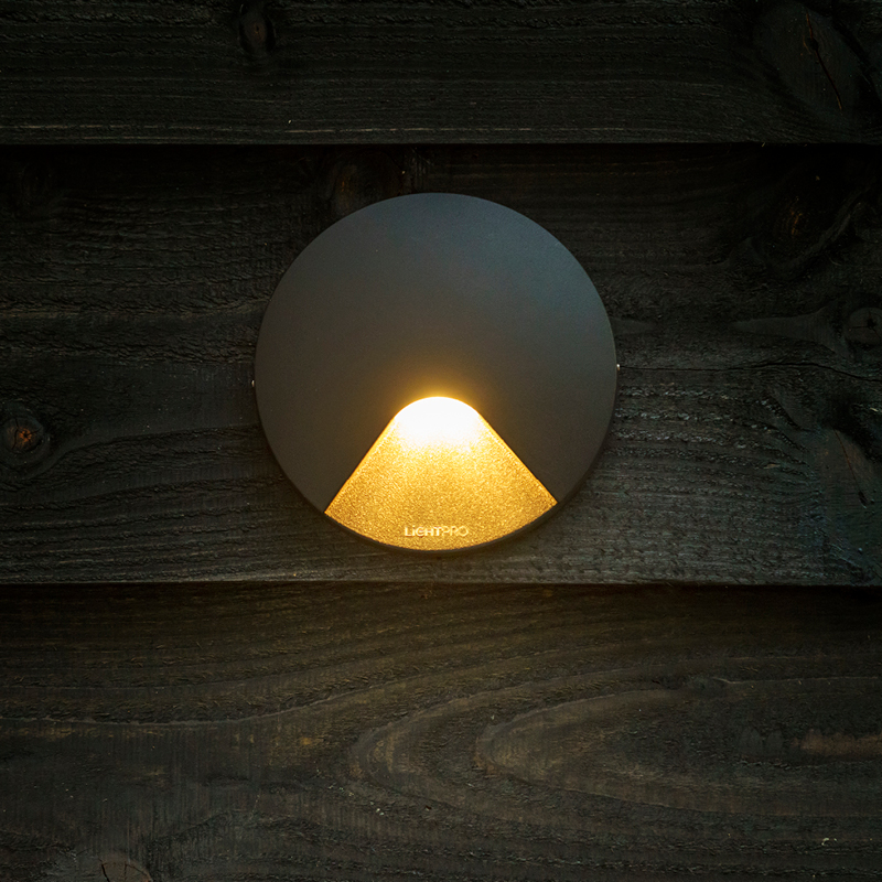 Lampe murale allumée sur bois foncé.